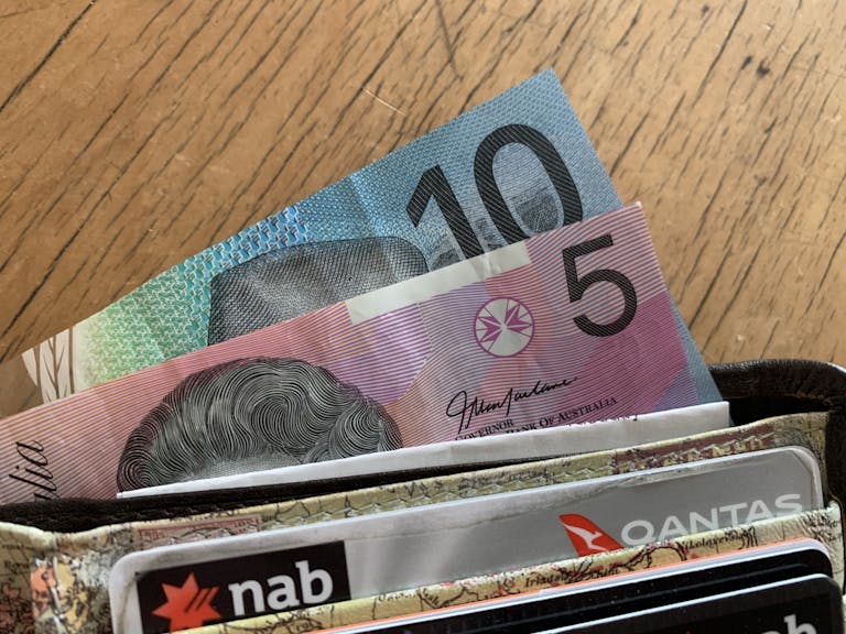 Close-up of Australian dollar bills and credit cards in a wallet on a wooden surface.
