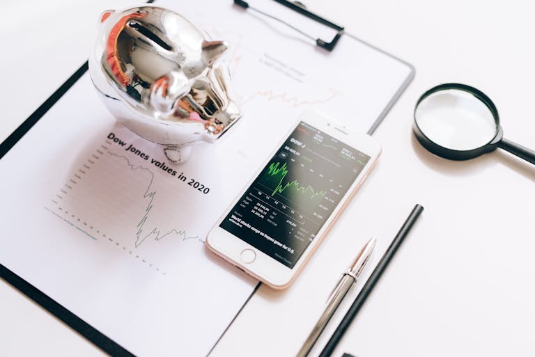 Flat lay of financial tools: chart, smartphone, magnifying glass, and piggy bank.